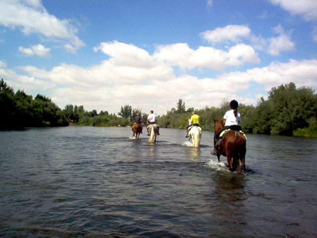Jinetes a caballo siguiendo el curso del río.